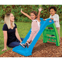 Children playing on a blue and green slide with a woman sitting nearby.