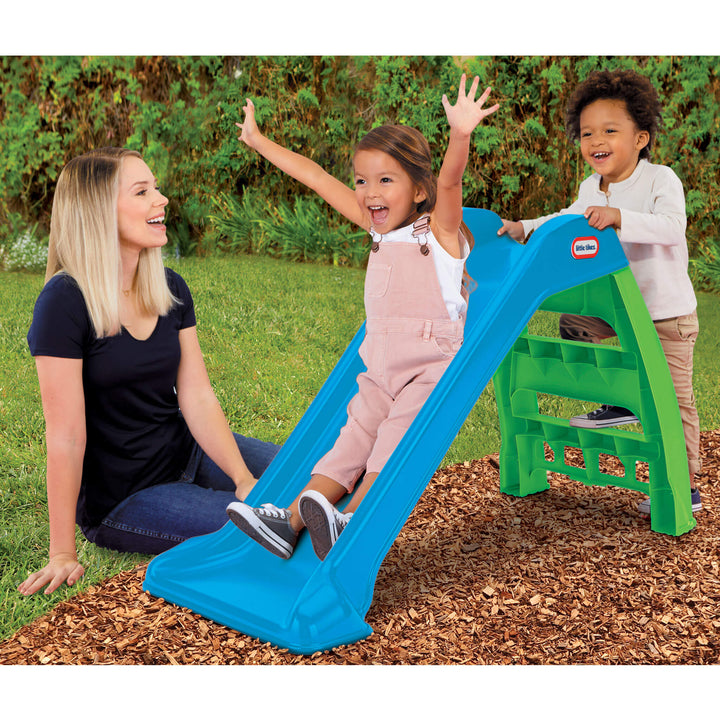 Children playing on a blue and green slide with a woman sitting nearby.