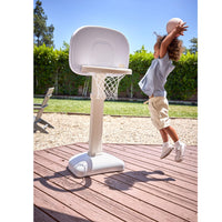 Child jumping to make a slam dunk outside on a brown deck with grass and trees in the background