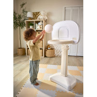 Child with brown curly hair, tan shirt and blue jeans tossing a ball into the hoop. 