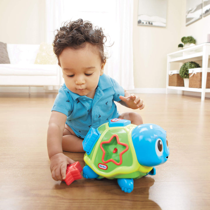 Child playing with a toy turtle on a wooden floor