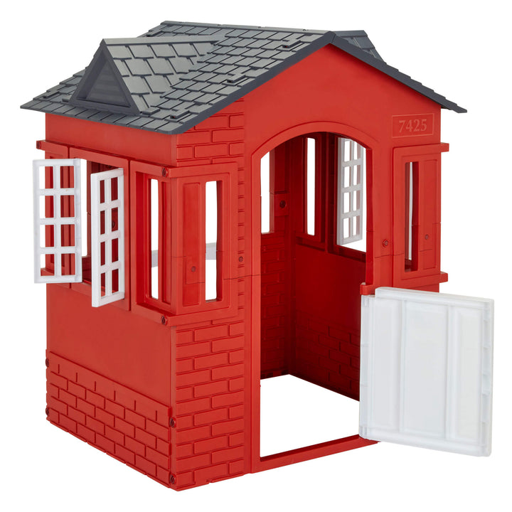 A red plastic playhouse with a dark gray shingled roof, white window frames, and a white door panel that is swung open, shown on a plain white background.