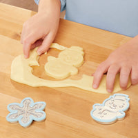 Hands shaping cookie dough with snowflake and snowman cookie cutters on a wooden table.