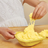 Child playing with yellow play sand on a wooden table