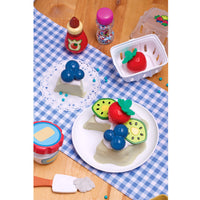 food set on a checkered tablecloth with various toy fruits and containers.