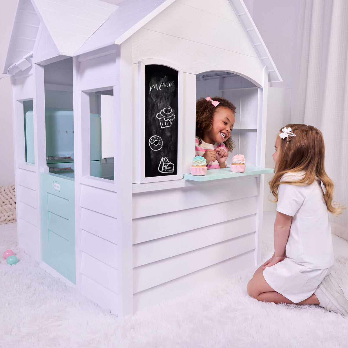 Two girls, one inside the white house the other outside using the open window talking, with two cupcakes sitting on the Sea Foam green ledge. Chalkboard is to the left of the girls, in front is Sea Foam green door.