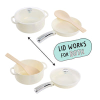 Four-piece toy cookware set with cream-colored pots and pans, silver handles, and light wood spoons, shown on a white background with an arrow and text indicating the lid works for both pots and pans.