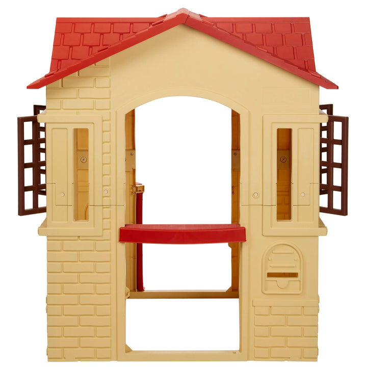 A playhouse shaped like a small house with a beige brick-textured body, red tiled roof, and brown shutters, shown on a plain white background.