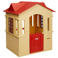 A playhouse, with a red tiled roof, cream-colored brick walls, and a red front door. The Little Tikes logo is visible on the door.