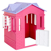 A pink plastic playhouse shaped like a small house with a purple roof, white window frames, and a white door, shown on a plain white background.