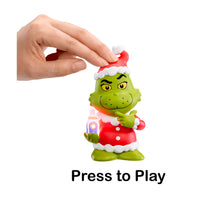 Toy figure of Santa Grinch holding a Story Dream Machine with a hand pressing a button labeled 'Press to Play'.