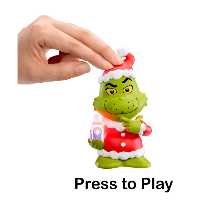 Toy figure of Santa Grinch holding a Story Dream Machine with a hand pressing a button labeled 'Press to Play'.