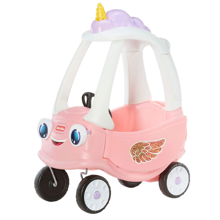 A pink toy ride-on car with a smiling face, large blue eyes, black wheels, a white roof frame,  and a gold wing decal on the side.