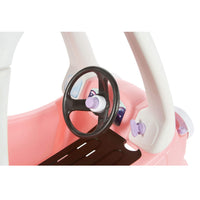 Close-up of a children's toy car interior with a pink body, white steering column, black steering wheel, and small purple accents on a white background.