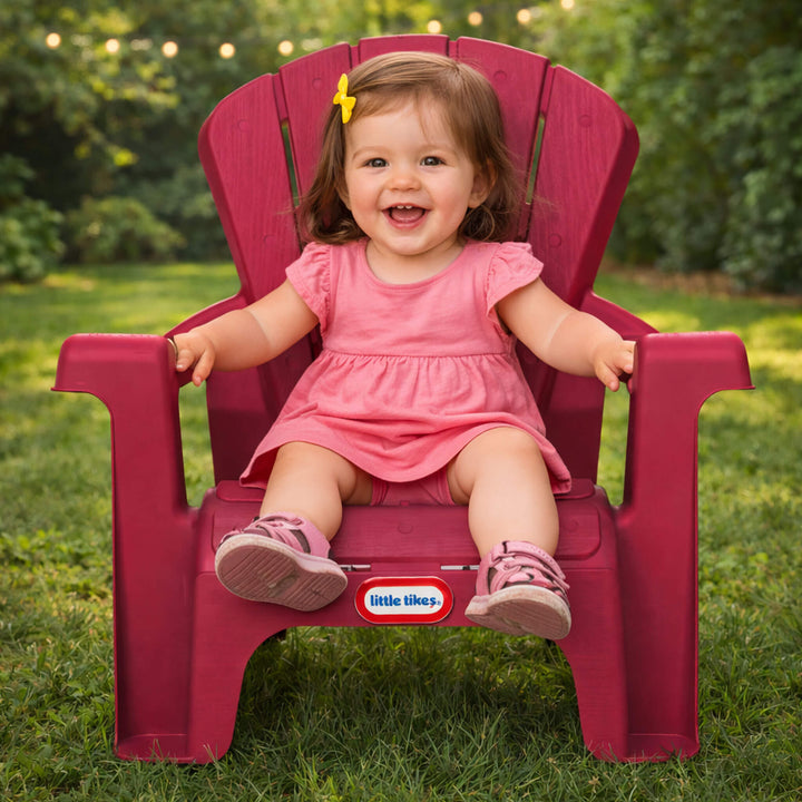 Child in a pink dress sitting on a red chair with 'Little Tikes' logo outdoors.