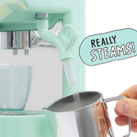 A mint green espresso machine being used to steam water in a pitcher held by a hand. A speech bubble says 'REALLY STEAMS!'.