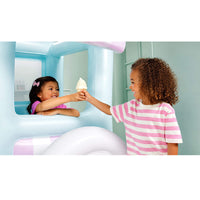Two children interacting with a light blue inflatable ice cream truck play structure. One child is inside the truck window holding a pink shirt, and the other child outside is handing an ice cream cone to her.