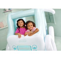Two young girls smiling and posing inside a light blue and white inflatable truck-shaped, in a pale green room. The Little Likes brand logo is visible on the front of the inflatable.