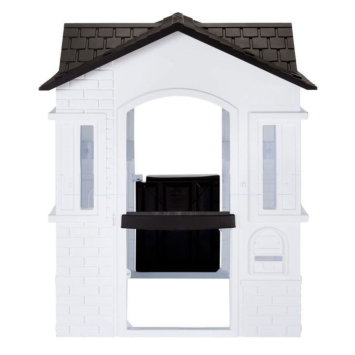 A white plastic playhouse with a black tiled roof featuring an open back with a mail slot isolated on a white background.