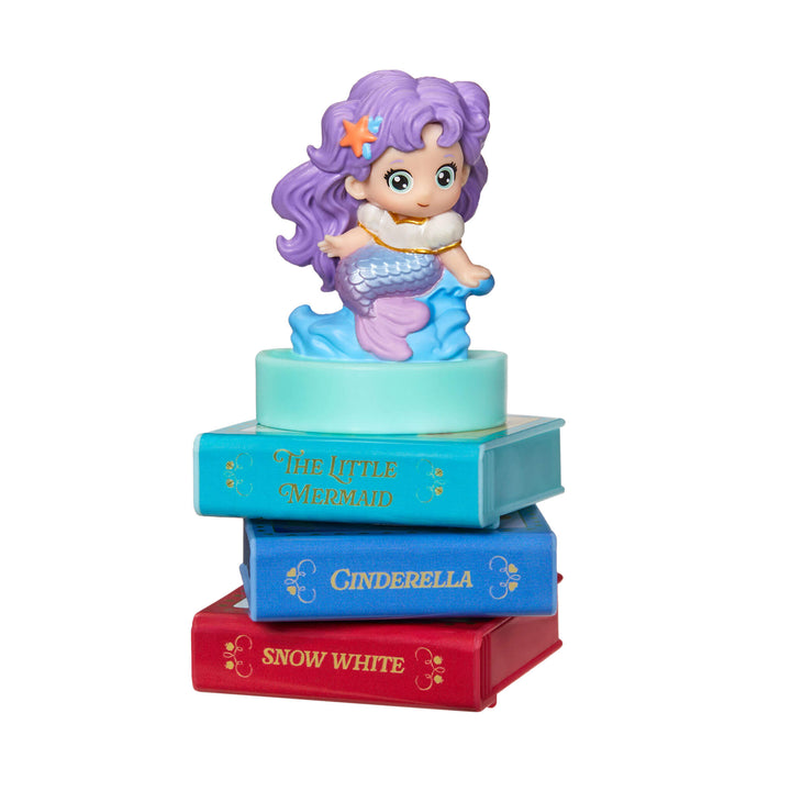 Stack of children's books ’The Little Mermaid’, Cinderella and Snow White with a toy Mermaid on top against a white background