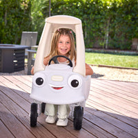 Child with long blonde hair sitting in the white Coupe on a wood deck with trees in the background