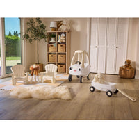 Indoor setting with the White Cozy Coupe, white wagon with a stuffed bunny sitting in side, two white garden chairs with beige walls and a bookcase in the background