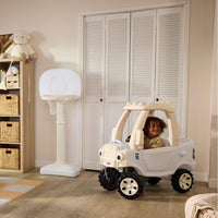 Child sitting in he White Cozy Truck with beige roof in a playroom setting with beige walls and a white and beige basketball hoop