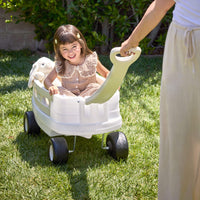 Child sitting in white wagon being pulled on grass