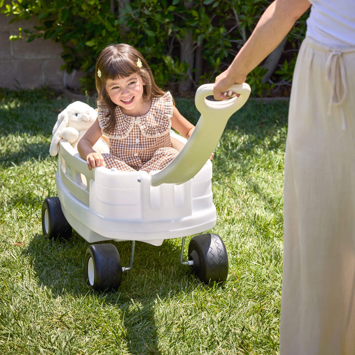 Child sitting in white wagon being pulled on grass