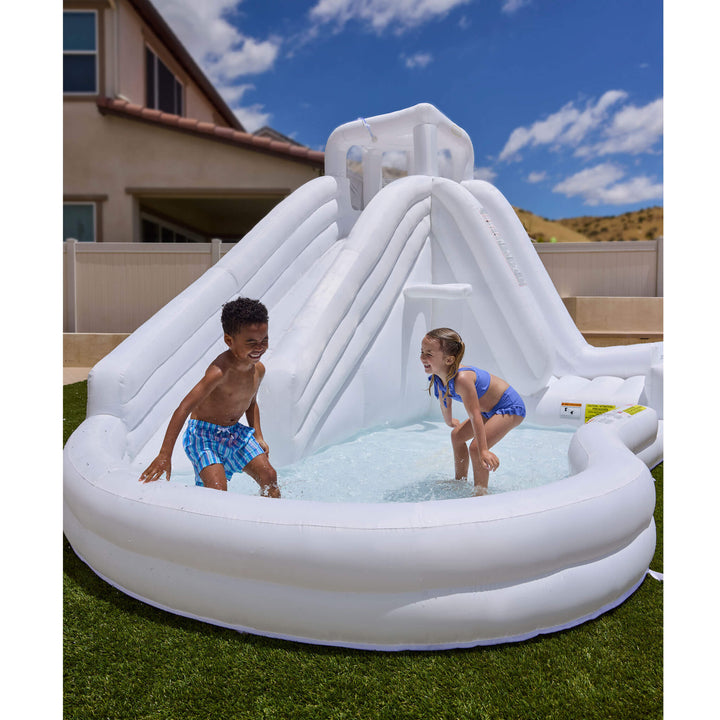 An inflatable outdoor water slide pool with a shallow pool at the base, shown on a lawn with two children playing under a blue sky. 