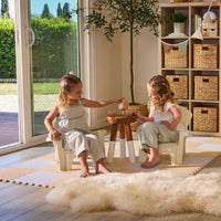 Two girls having a tea party sitting on the chairs, with a small table between them, in a playroom setting with beige walls
