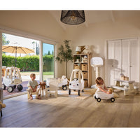 Indoor setting with child sitting on a white garden chair, white basketball hoop, white Cozy Coupe, white wagon with a white Cozy truck outside