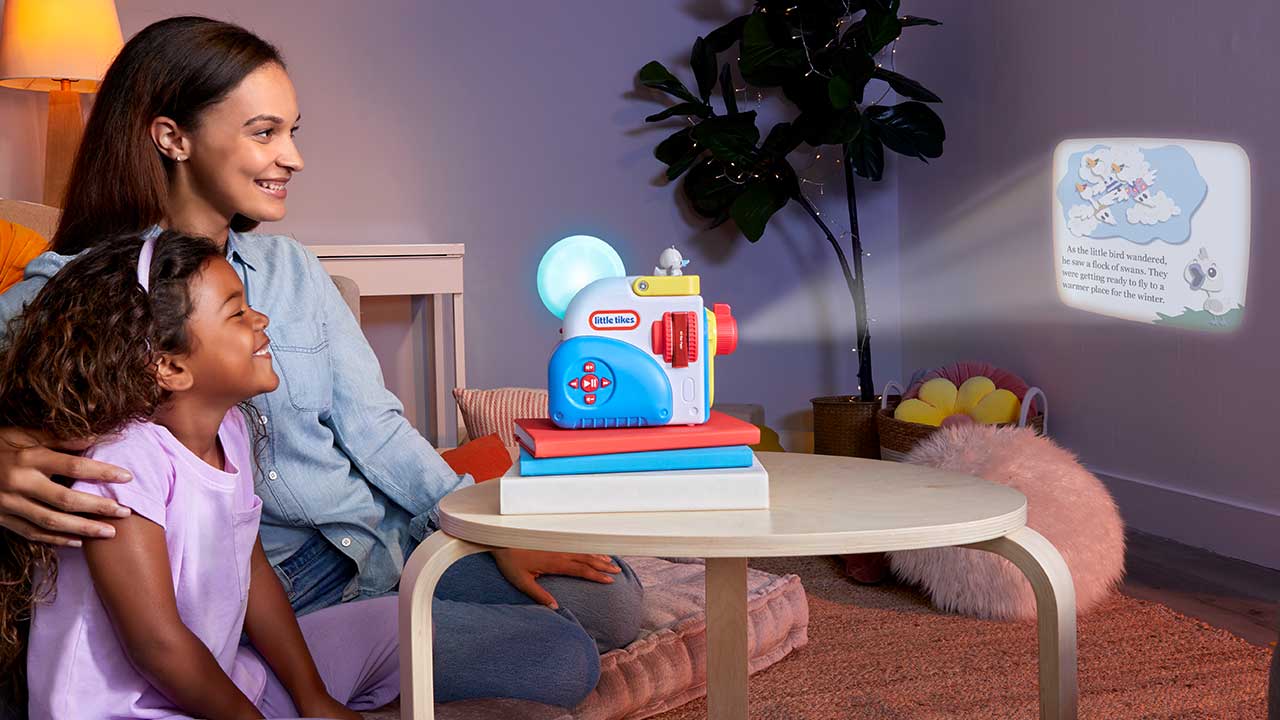 Woman and child sitting at a table with a The Story Dream Machine and a screen displaying educational content.