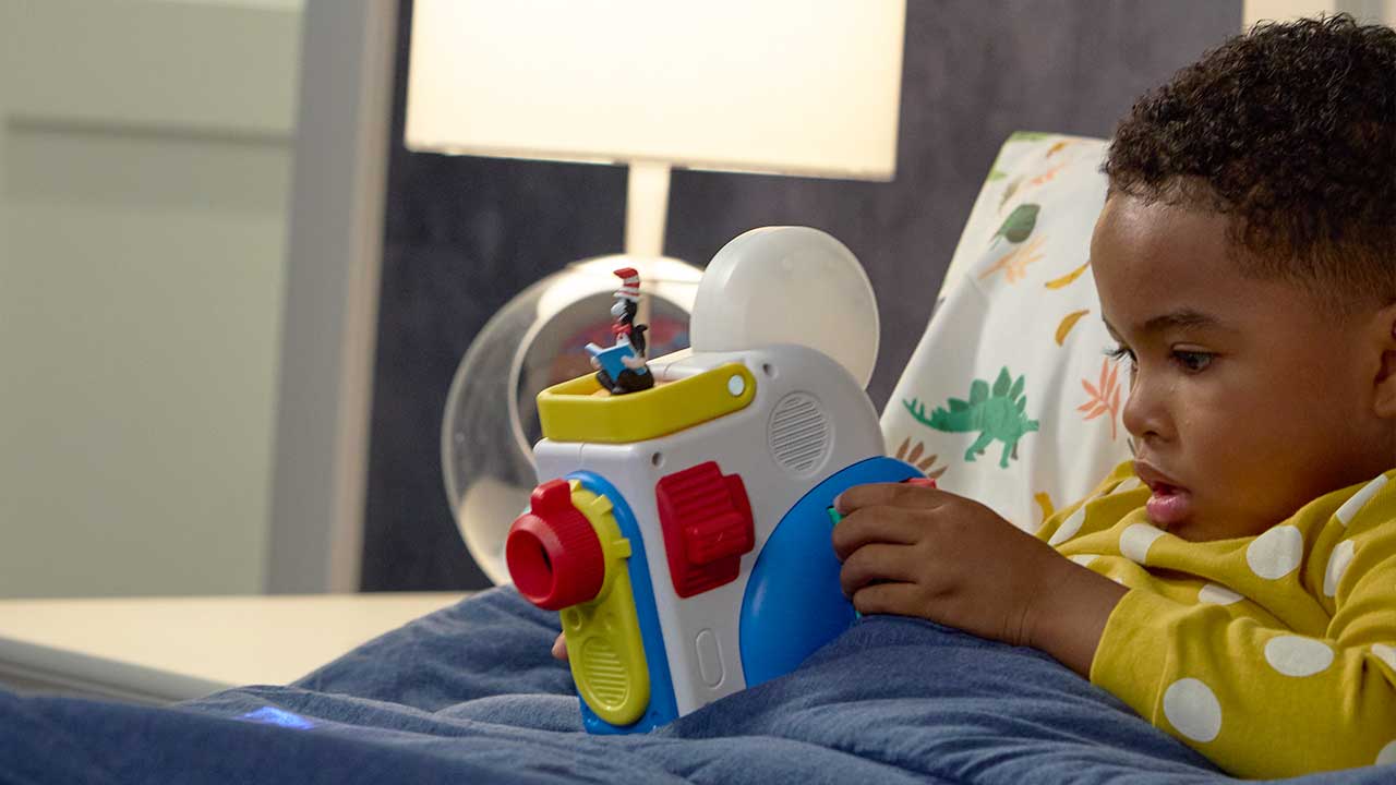 Child playing with a Story Dream Machine train on a bed