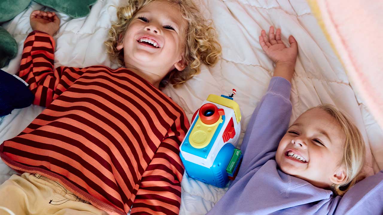Two children lying on a bed with a Story Dream Machine between them