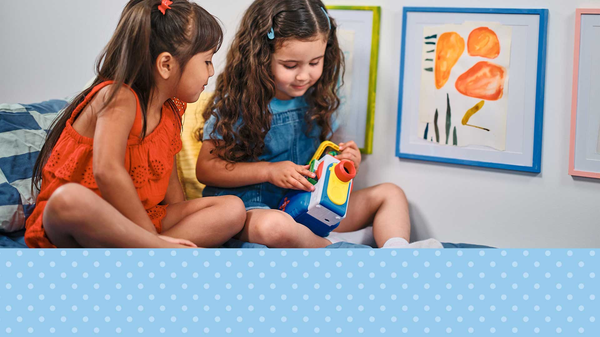 Two young girls playing with a toy on a bed in a bedroom.